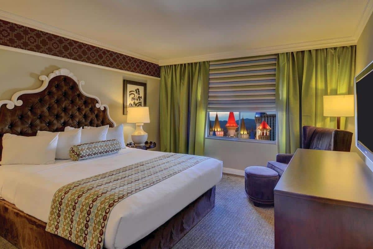 Quarto do Excalibur com uma cama de casal, de frente para um móvel e uma TV. Ao fundo está uma janela com vista para o topo do hotel, que se assemelha a um castelo.