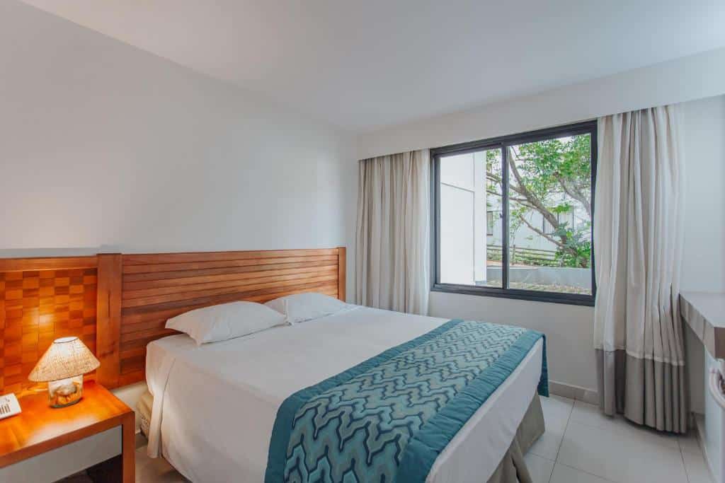 Quarto simples e aconchegante do Hotel Luupi com cama de casal, iluminação suave e vista para a área verde. Um dos hotéis no Rio Quente Resorts.