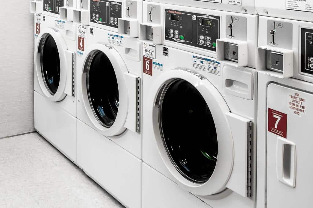 A lavanderia do hotel courtyard by Marriott New York Manhattan tem uma fileira de máquinas de lavar e secar brancas. Cada máquina possui um painel de controle digital na parte superior. As máquinas estão alinhadas ao longo de uma parede branca.