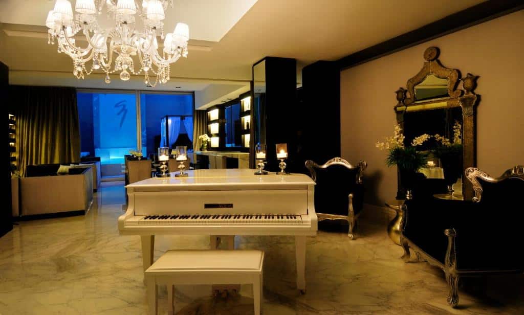 Uma luxuosa sala de estar com um piano de cauda branco, lustre, espelho ornamentado e piso de mármore, no 1828 Smart Hotel Boutique.