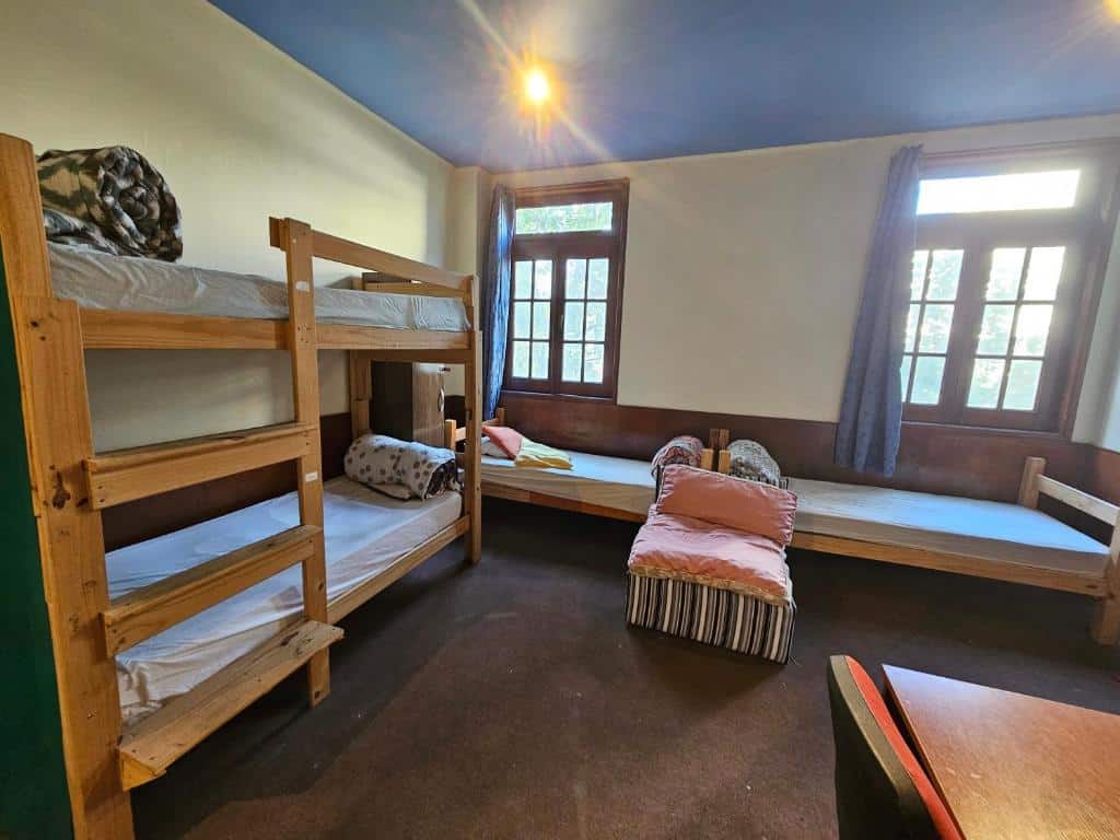 Quarto do Montevideo Hostel. Uma cama de beliche no canto esquerdo, no fundo duas camas de solteiro e janelas de vidro.