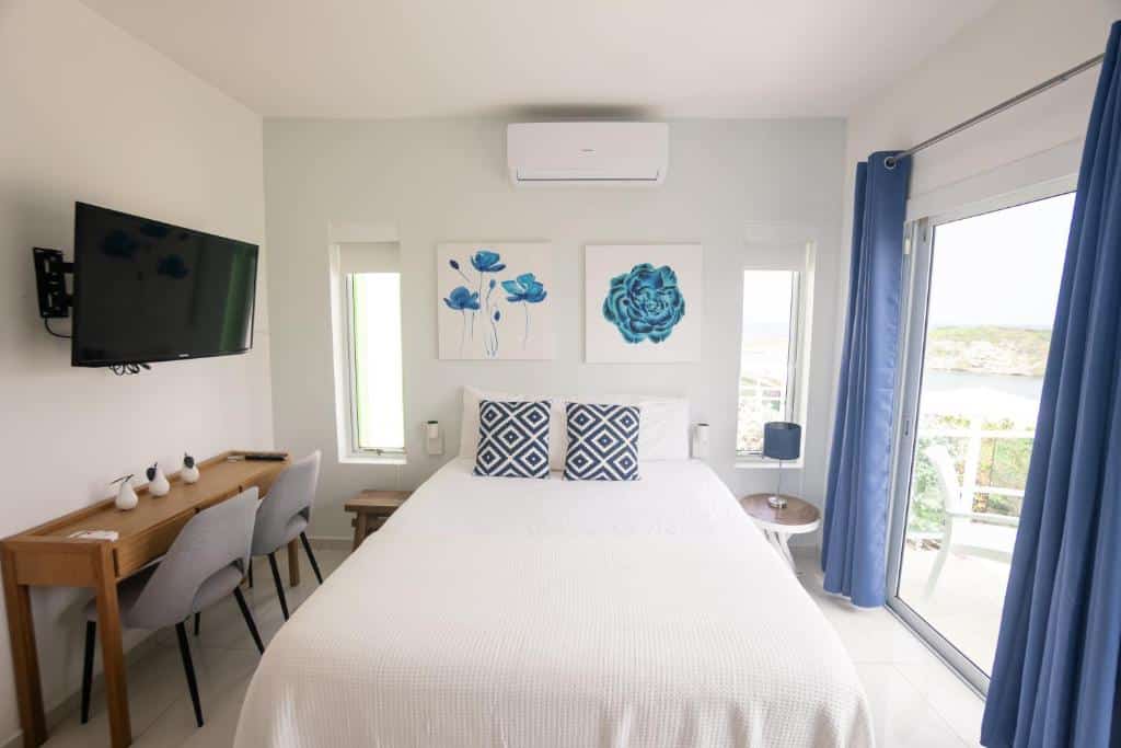 Quarto do Piscadera Harbour Village. Uma cama de casal e um ar-condicionado no centro, do lado esquerdo uma mesa de trabalha com duas cadeiras e uma TV. Do lado direito a porta da varanda.