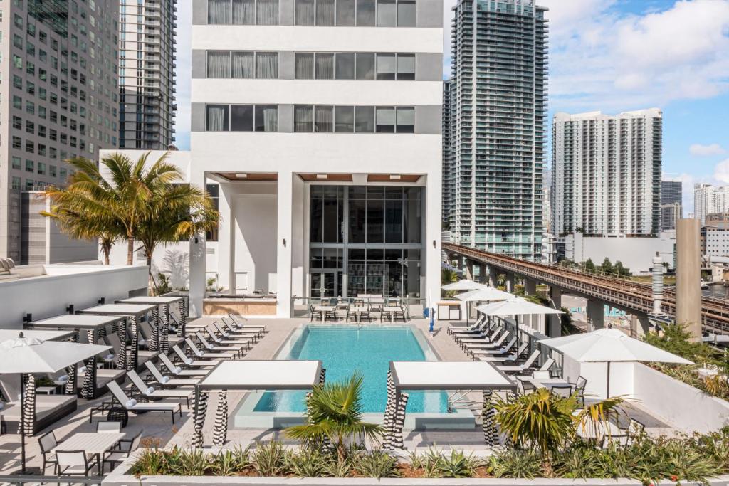 Área de lazer do Element Miami Brickell durante o dia com a piscina quadrada no centro e em cada lado da piscina cadeiras e ao fundo o hotel.