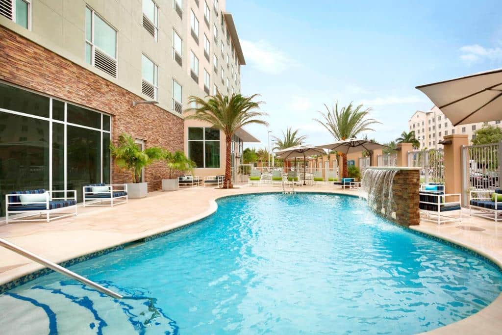 Área de lazer do Four Points by Sheraton Miami Airport durante o dia com piscina no centro e do lado esquerdo cadeiras estofadas.