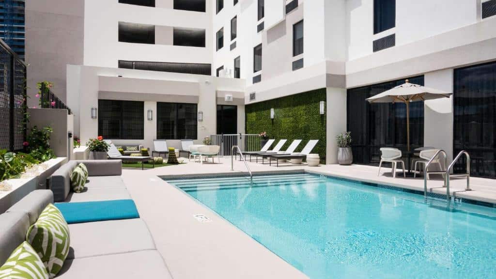 Área de lazer do Hampton Inn & Suites Miami Wynwood Design District, FL durante o dia com sofás do lado esquerdo da imagem do lado direito uma piscina quadrada e atrás da piscina cadeiras.