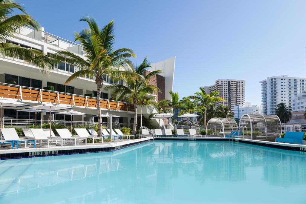 Área de lazer do The Gates Hotel South Beach – a Doubletree by Hilton durante o dia com piscina a frente e ao fundo cadeiras em volta e o edificio.
