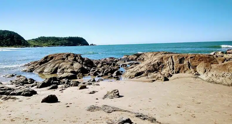 Imagem da praia de Paciência, em Penha durante o dia com o faixa de areia a frente com pedras e ao fundo o mar. Representa saiba o que fazer em Penha.