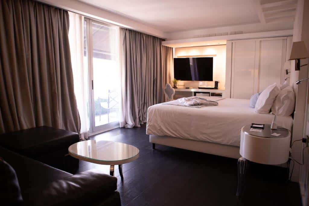 Quarto no 1828 Smart Hotel Boutique com uma cama king-size, TV, mesa redonda, sofá e janela grande com cortinas fechadas, para representar hotéis boutique em Buenos Aires.