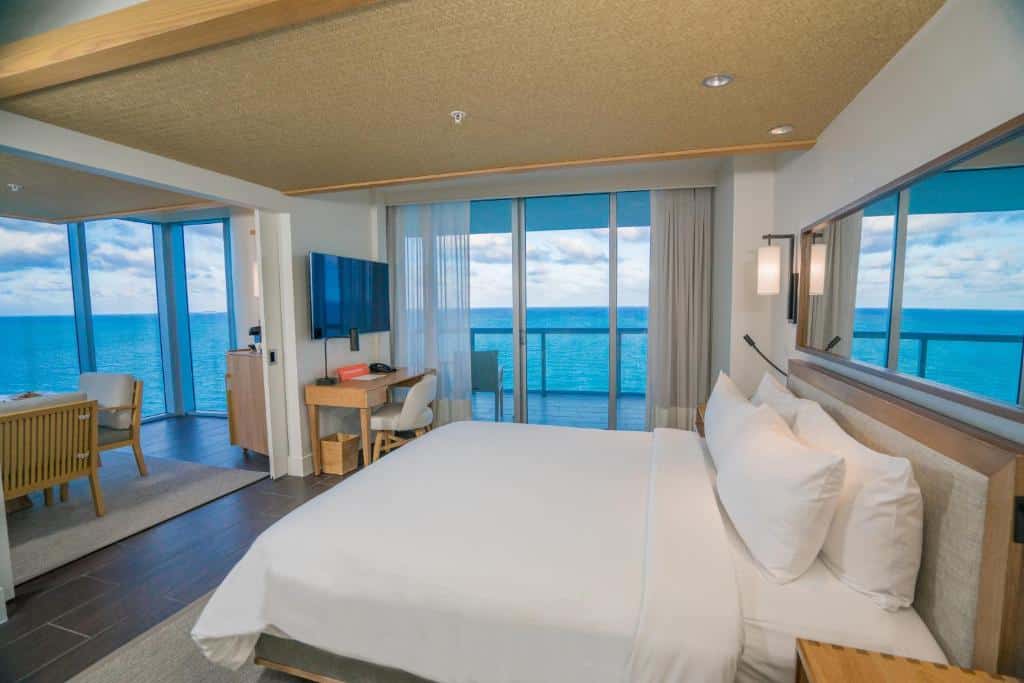 Quarto do Eden Roc Miami Beach com cama de casal do lado direito da imagem em frente a cama um jogo de sofá e do lado direito da cama a frente no canto uma mesa de trabalho com cadeira e preso na parede a TV. Representa resorts em Miami.