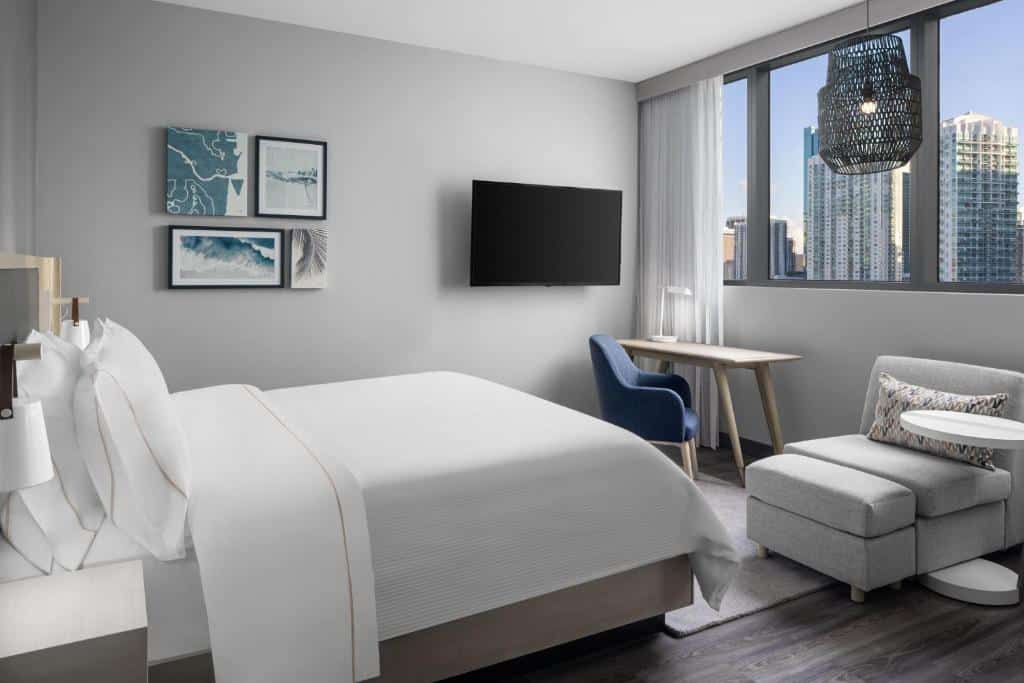 Quarto do Element Miami Brickell com cama de casal do lado esquerdo da imagem em uma poltrona e uma mesa com cadeira e do lado preso na parede uma TV. Representa hotéis 3 estrelas em Miami.