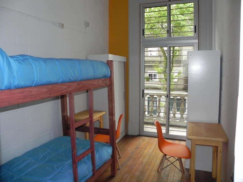 Quarto do Student’s Hostel. Uma cama beliche do lado esquerdo, de cada aldo uma mesa de trabalho e um guarda-roupa. No fundo uma porta de vidro para a varanda.