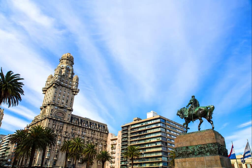 Palácio Salvo no fundo e na frente a praça com monumento e palmeiras.