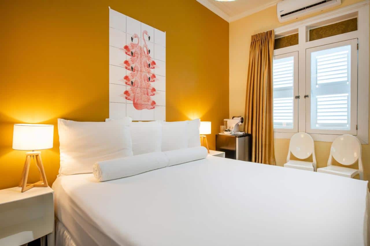 Quarto do Vila Amalie e Vila Curiel. Uma cama de casal de cada lado uma cômoda com abajur. No fundo um frigobar, a janela fechada, um ar-condicionado e duas cadeiras. Imagem para ilustrar post sobre hotéis em Curação.