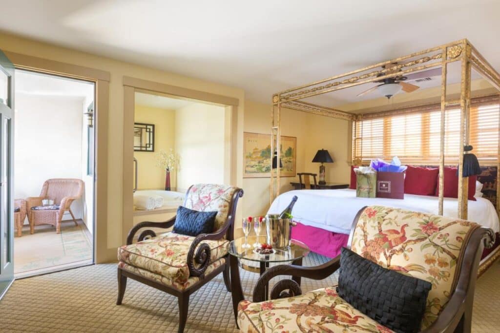 Quarto do 1906 Lodge. Uma cama com dossel está do lado direito, atrás de duas poltronas e uma mesinha de centro. Ao lado estão portas para a varanda e para o banheiro. Essa é uma opção incrível de onde ficar em San Diego.