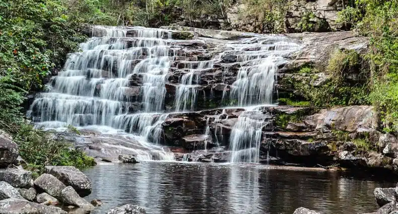 Pequena cachoeira no Vale do Pati caindo sobre saliências rochosas formando uma piscina calma, cercada por vegetação verdejante e pedras. A foto ilustra o post de o que fazer na Chapada Diamantina.
