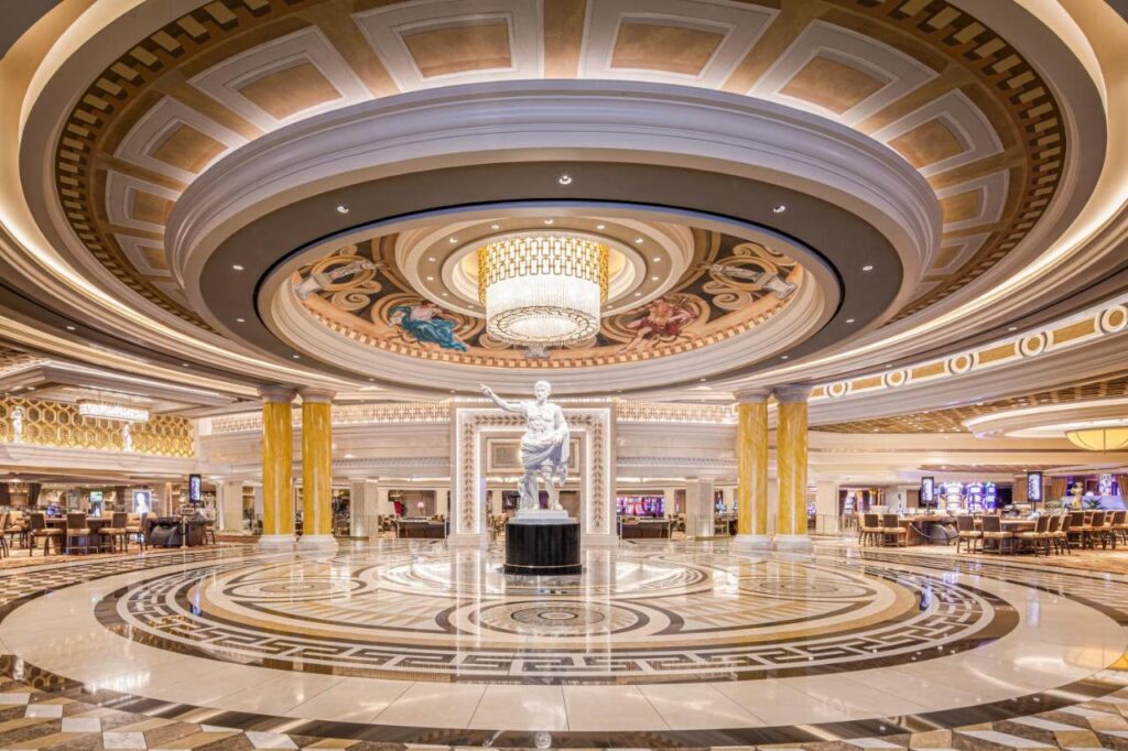 Luxuoso lobby do Caesars Palace com uma estátua central, teto ornamentado, grande lustre e padrões decorativos no piso. A foto ilustra o post de cassinos em Las Vegas.