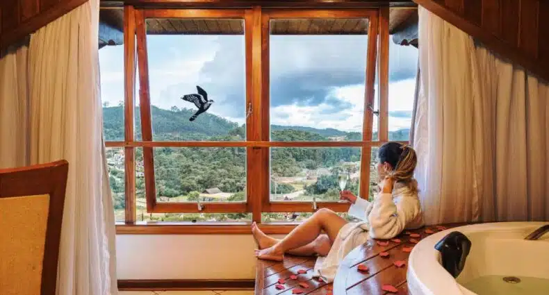Imagem de uma banheira de hidromassagem do lado direito a frente e ao fundo uma mulher no Carícia do Vento Pousada Boutique do lado direito sentada vendo as montanhas. Representa chalés em Monte Verde.
