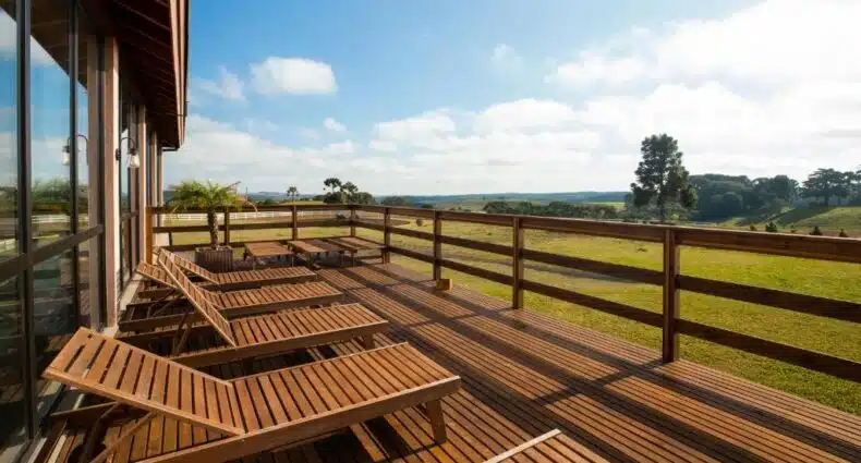 Imagem da varanda do Cerro Azul Hotel Fazenda durante o dia com cadeiras do lado esquerdo com vista para o jardim. Representa hotéis fazenda na Serra Catarinense.