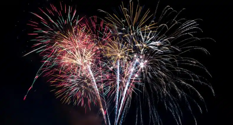 Uma série colorida de fogos de artifício explode contra um céu escuro, com explosões de faíscas vermelhas, verdes, azuis e amarelas.