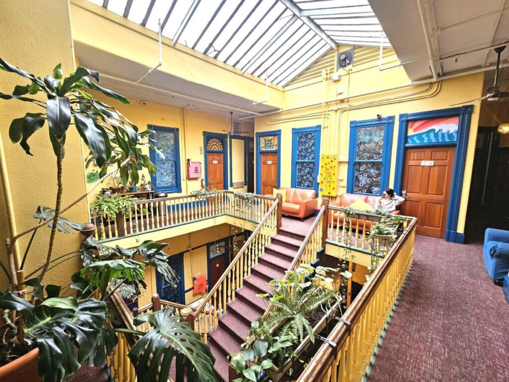 Área comum do Gaslamp Hostel. Uma grande escada está no meio da imagem. Na parte de cima estão dois sofás e algumas portas. Foto para a lista de onde ficar em San Diego.