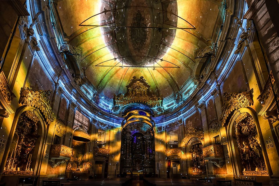 O interior da Igreja dos Clérigos ornamentada com tetos altos é iluminado com luzes coloridas e vibrantes, criando uma atmosfera dramática e envolvente.