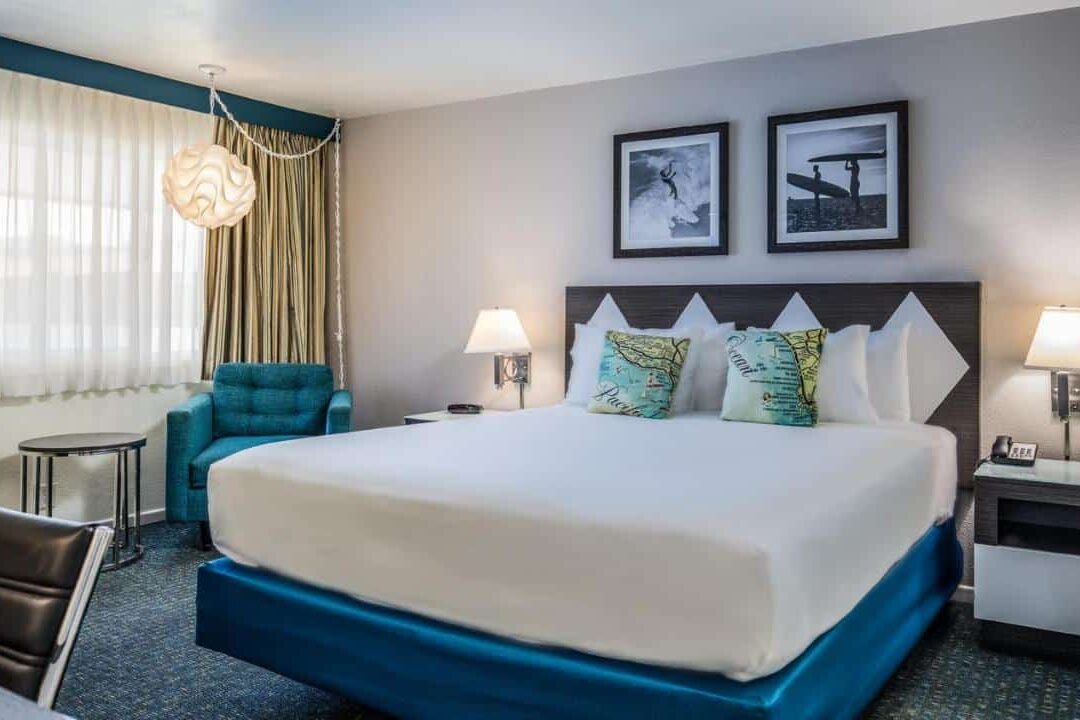 Quarto do Kings Inn com uma cama de casal ao lado de uma poltrona e uma janela. Ao lado direito está uma mesinha com abajour.