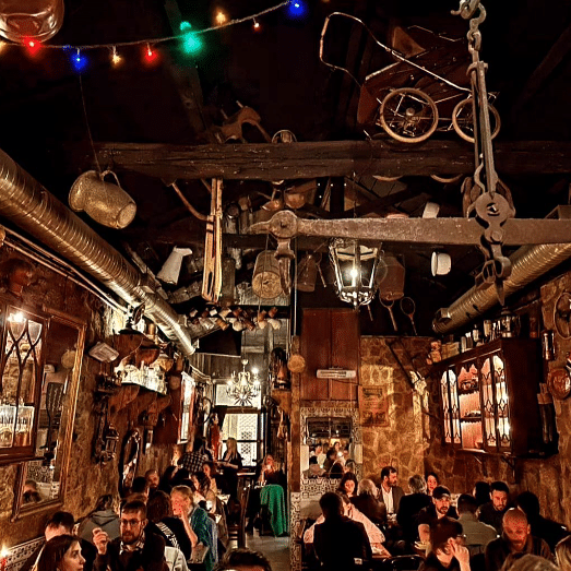 Restaurante rústico do Museu D’ Avó com pouca iluminação, com vários itens vintage pendurados no teto e nas paredes; os clientes estão jantando em várias mesas.