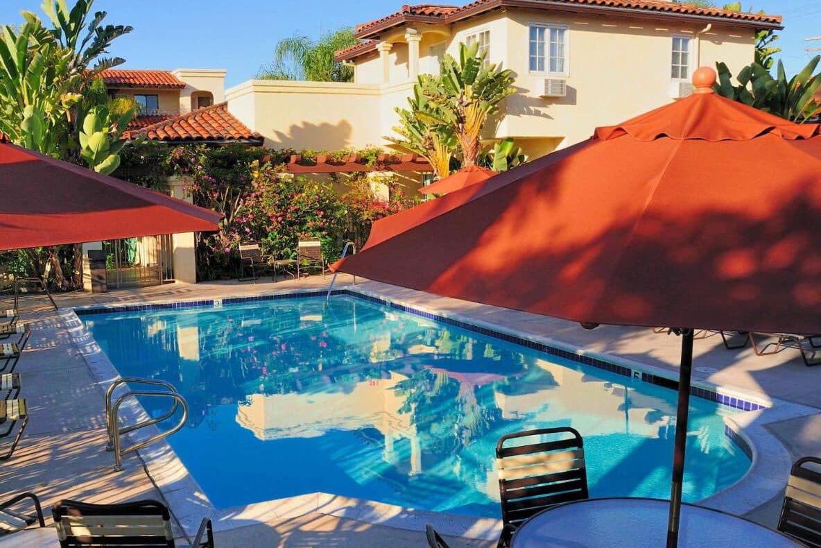 Piscina do Old Town Inn. Ela está no meio de uma área aberta, entre vários gaurda-sóis, mesas e cadeiras. Essa é uma ótima opção de onde ficar em San Diego.