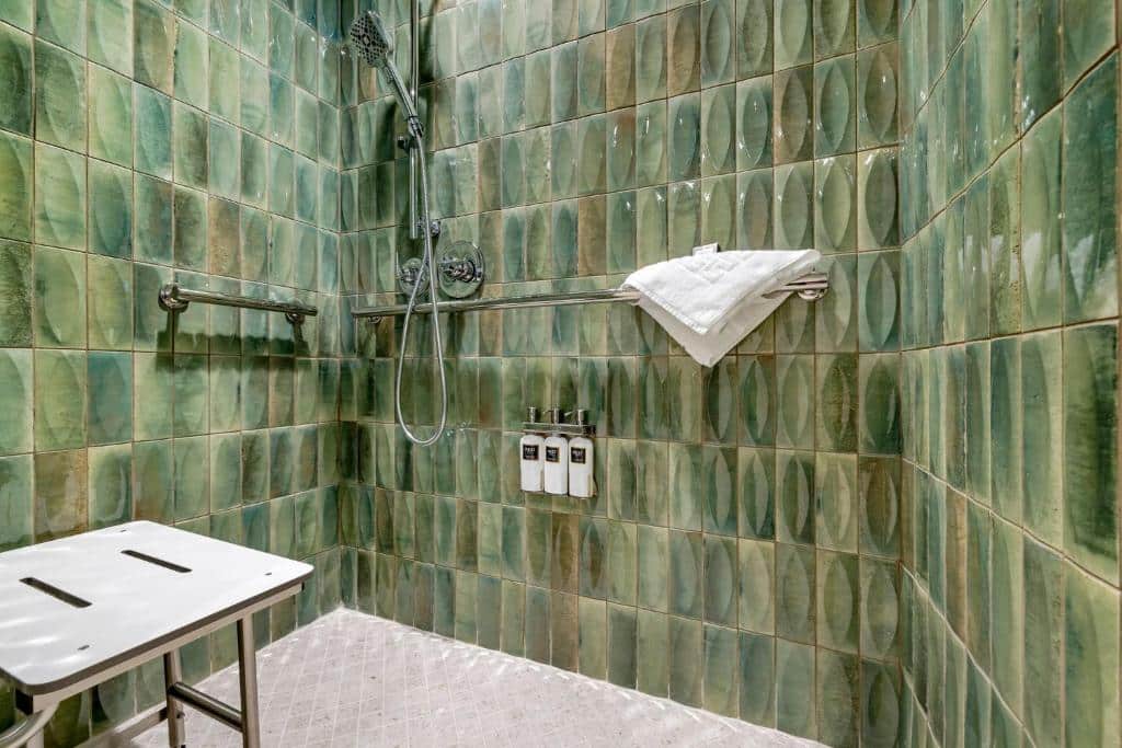 Banheiro acessível do Omni San Diego Hotel. Um banco para banho está no canto esquerdo. Na parede do lado direoto, onde fica o chuveiro, estão duas barras de apoio.