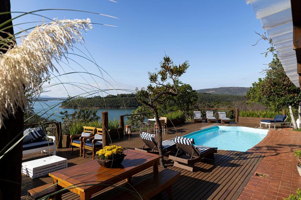 Terraço ao ar livre da Pousada Cachoeira Lagoa Azul com deck de madeira, piscina, espreguiçadeiras e área de jantar com vista para um lago e colinas distantes.