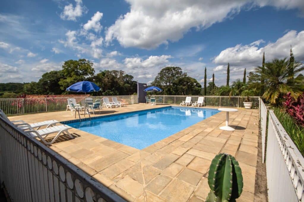 Piscina ao ar livre da Pousada Vegas, com cadeiras e guarda-sóis ao redor.