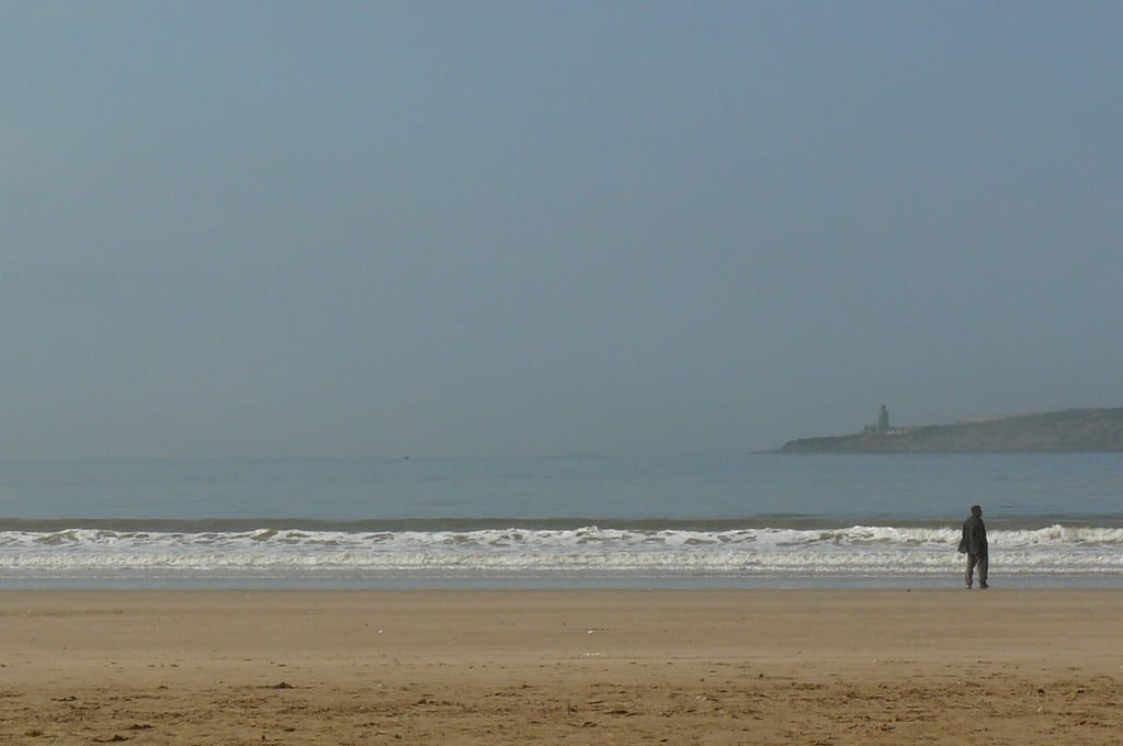 Somente um homem no canto direito na beira do mar na praia de Essaouira. Imagem para ilustrar post sobre o que fazer no Marrocos.