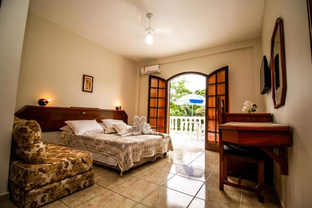 Quarto do Mata Atlântica Park Hotel com cama de casal do lado esquerdo da imagem do lado direito da cama um sofá e em frente a cama uma cômoda com cadeira.