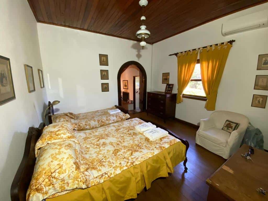 Imagem de um quarto familiar da Pousada Fazenda Pinhalzinho com uma cama de casal do lado esquerdo e do lado esquerdo da cama uma cama de casal e em frente a cama de casal uma poltrona.