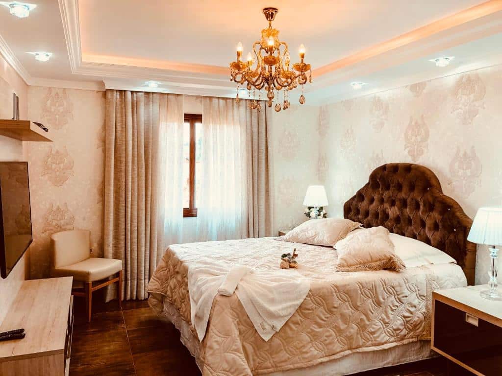 Quarto do Hope Valley Adventure Resort com cama de casal do lado direito da imagem em cada lado da cama uma cômoda com luminária em frente a cama uma cômoda com TV presa na parede e do lado esquerdo da cômoda uma cadeira. Representa dos hotéis fazenda no Paraná.