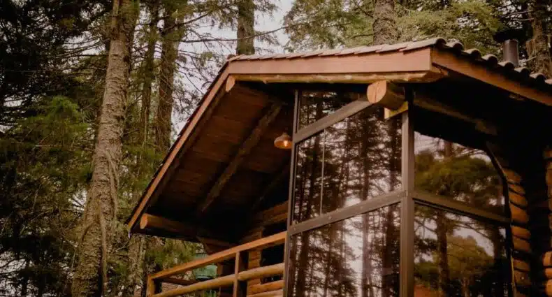 Imagem do chalé Refúgio do Crcol Pipas e Chalés, feito de madeiras e uma porta frontal de vidro. Está em meio de várias árvores em Canela, no Rio Grande do Sul.