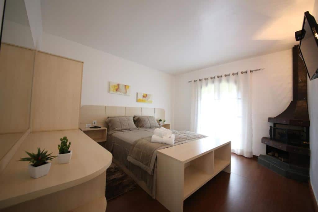 Quarto do Spazio di Garda. Uma TV e uma lareira do lado direito. Do lado esquerdo uma cômoda com espelho, no centro uma cama de casal.