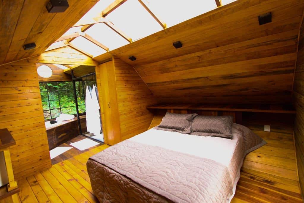 Quarto do Viva Brotas. Uma cama de casal na frente, no fundo roupões de banho e uma banheira.