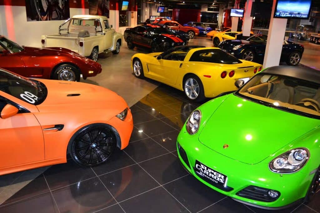 Showroom com vários carros esportivos, incluindo modelos laranja, verde, amarelo e vermelho, expostos em um piso de ladrilho brilhante na atração Super Carros em Gramado.