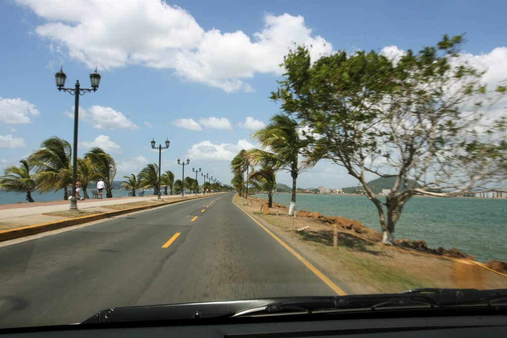 Estrada à beira-mar da Calçada de Amador com palmeiras em um dia ensolarado. Pessoas andam pela calçada. Essa é uma das opções de o que fazer na Cidade do Panamá.