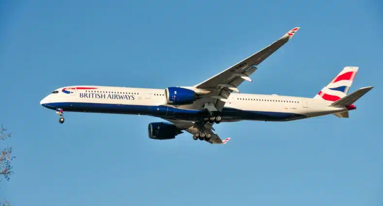 Um avião da British Airways voando contra um céu azul claro, com o trem de pouso abaixado e as asas estendidas. Representa como é voar de British Airways.