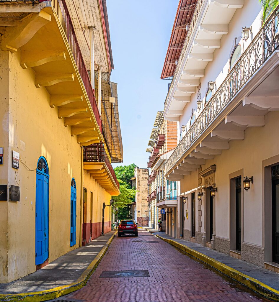 Essa é uma rua estreita em Casco Viejo. Ela é de paralelepípedos com edifícios coloridos e um carro estacionado sob um céu azul claro. A foto está na lista de o que fazer na Cidade do Panamá.