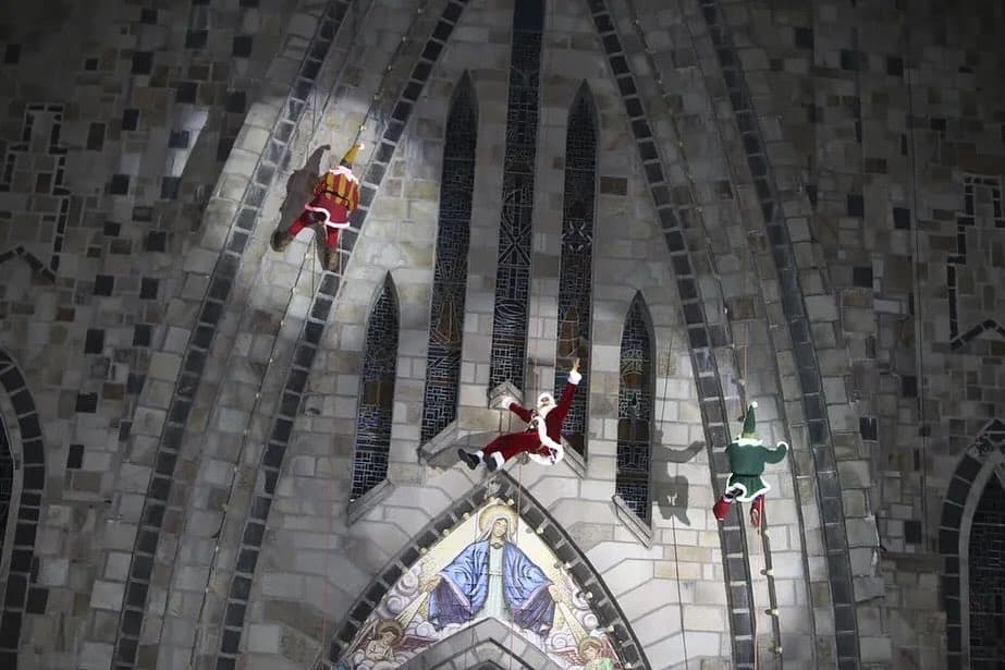 Uma pessoa vestidas de Papai Noel e duas vestidas de duendes descem pelo muro da Catedral de Pedra em Canela com cordas e arreios, acima de um vitral.