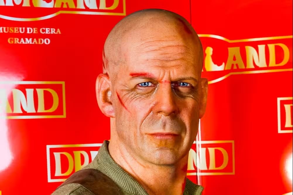 Figura de cera de um homem careca com expressão séria, o Vin Diesel vestindo uma camisa verde, sobre um fundo vermelho com texto amarelo no Museu de Cera uma das opções de o que fazer em Gramado.