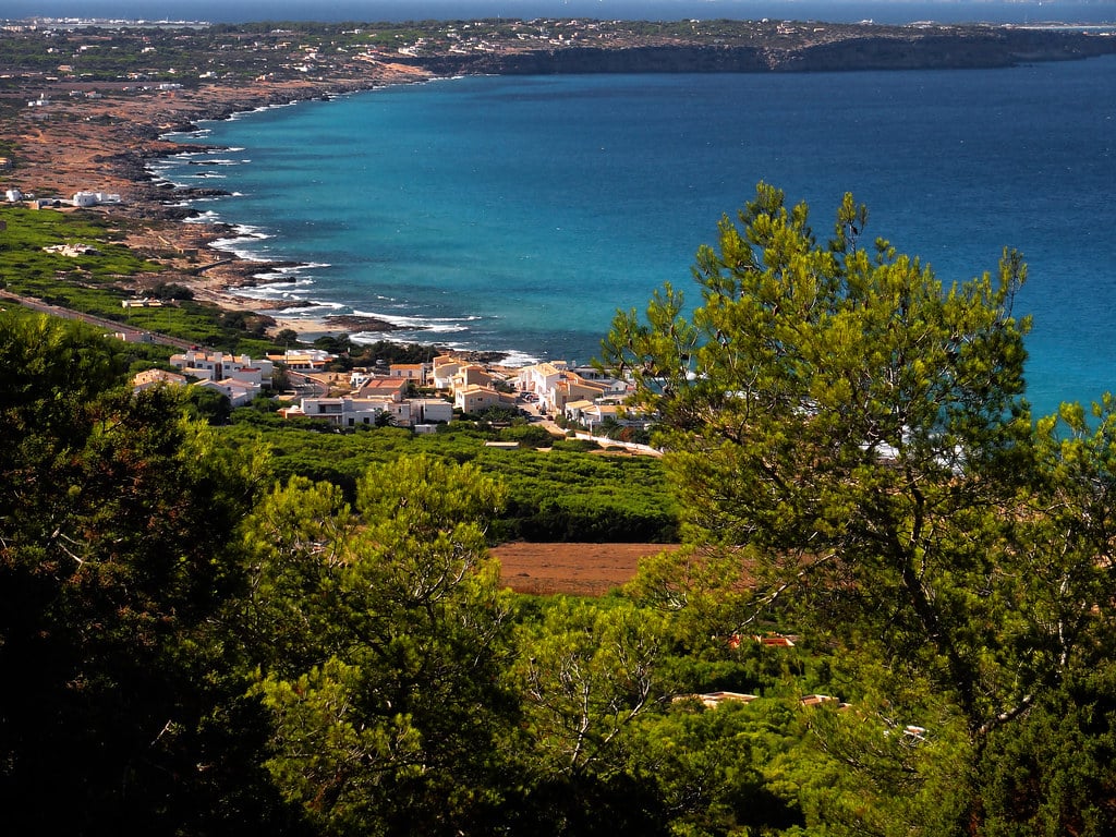 Uma vista costeira de El Mirador com águas azul-turquesa, um litoral com vegetação e um pequeno aglomerado de edifícios perto da costa sob um céu limpo.
