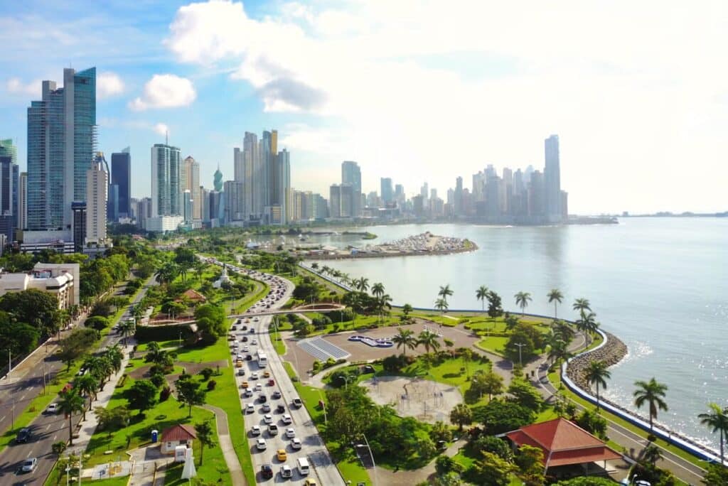 Vista aérea da paisagem urbana costeira da Cidade do Panamá com arranha-céus modernos, uma estrada sinuosa, espaços verdes e uma baía sob um céu limpo. Ele está na lista de o que fazer na Cidade do Panamá.