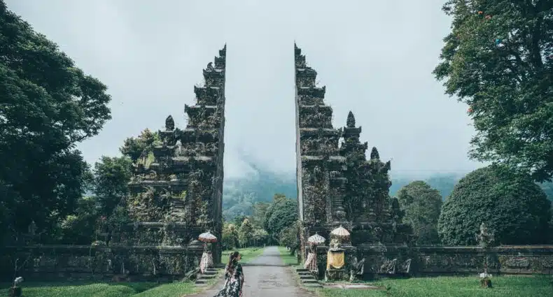 Imagem do arco de Handara Gate em Bali durante o dia com uma mulher a frente andando e ao fundo o arco. Representa Bali.