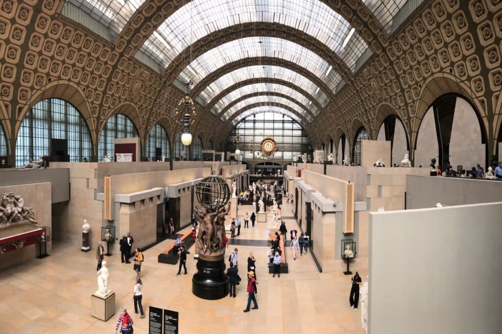 Pessoas caminhando no salão central do Museu d'Orsay, que tem tetos abobadados, esculturas e elementos decorativos.