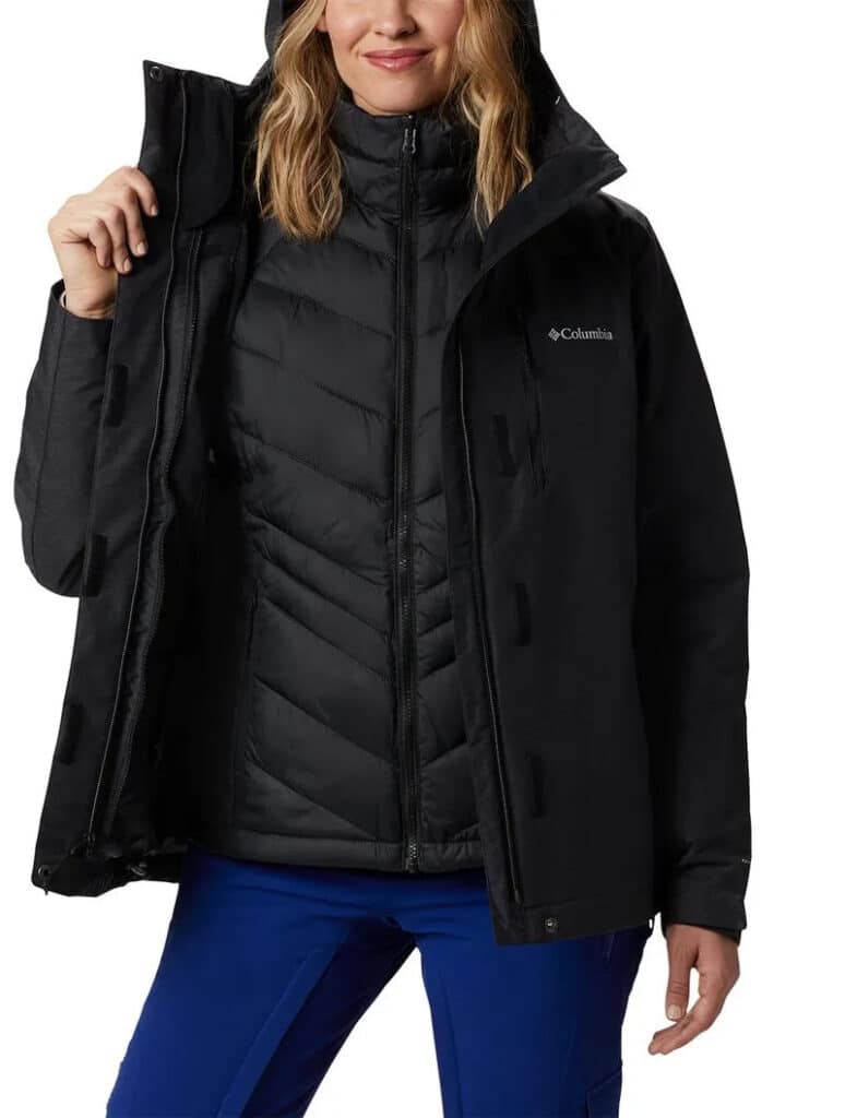 Uma pessoa vestindo uma jaqueta preta da Columbia com capuz sobre uma jaqueta acolchoada, segurando a jaqueta aberta para revelar as camadas.