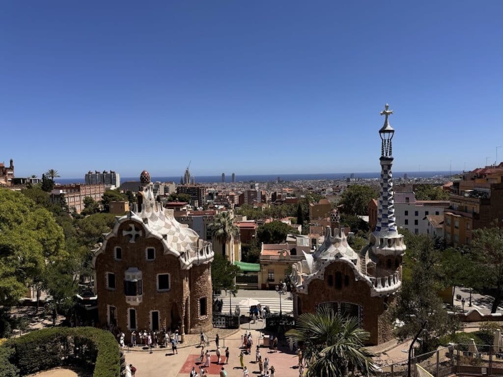 Uma vista do Parque Güell em Barcelona, mostrando estruturas arquitetônicas únicas e a paisagem urbana sob um céu azul claro.